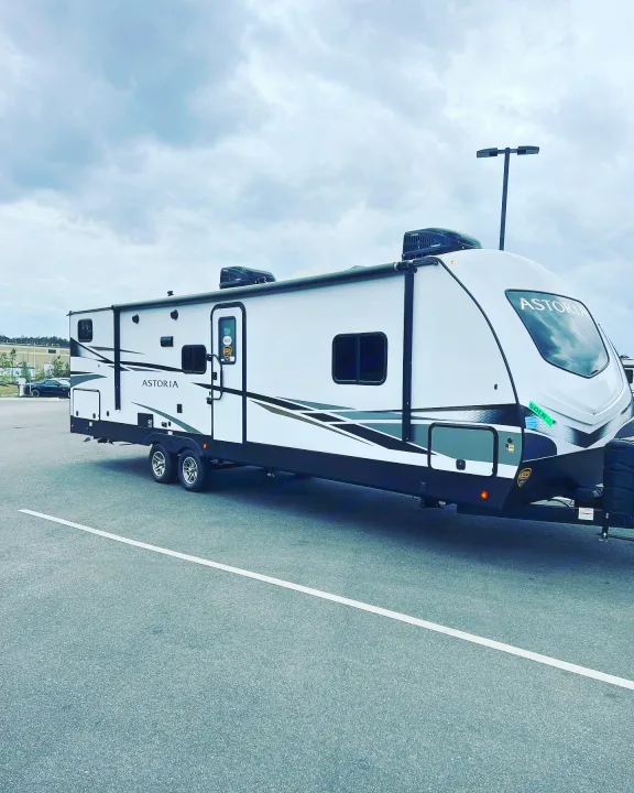 A white Astoria travel trailer, marked SOLD, parked outdoors under a cloudy sky. Explore an RV rental like this for your next trip.. Keystone RV Astoria 2903BH 2022