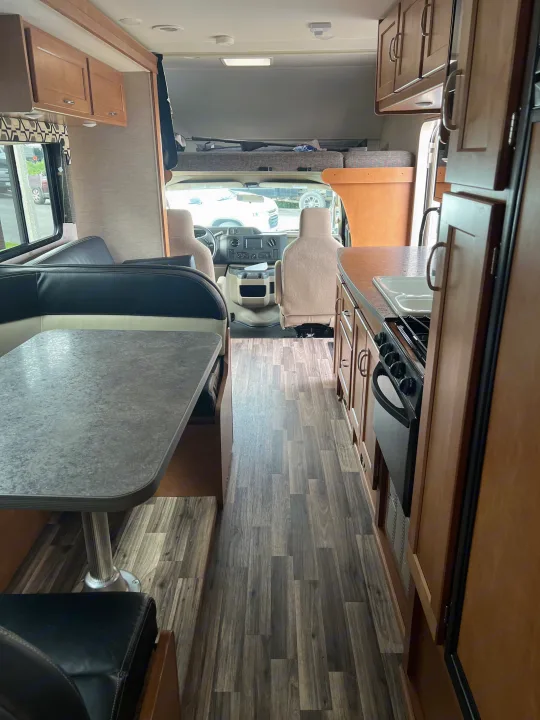 Spacious rv rental interior with wood-look flooring, showing kitchenette, dinette, and cab-over bunk, looking forward.. Winnebago Minnie Winnie 2016