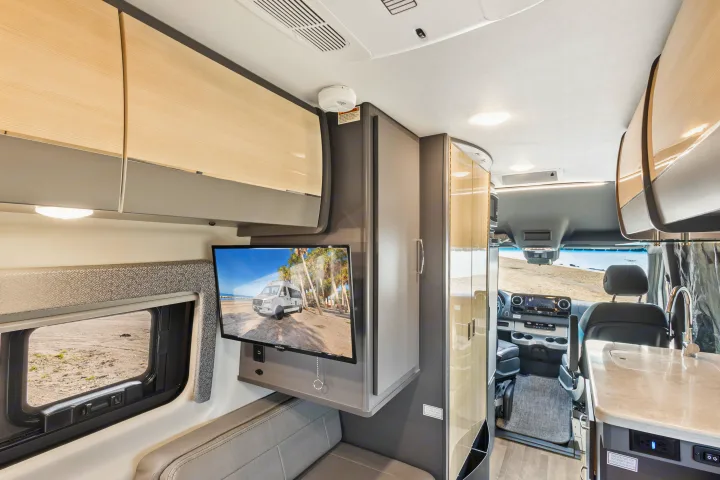 The modern interior of an **rv rental**, featuring a mounted TV, comfortable seating, kitchen counter, and driver's cabin.. Thor Sanctuary 2023