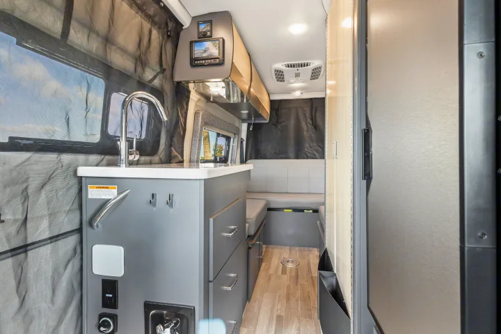 Inside this modern RV rental van: a sleek kitchen with sink and controls, plus comfortable dinette seating for adventure.. Thor Sanctuary 2023