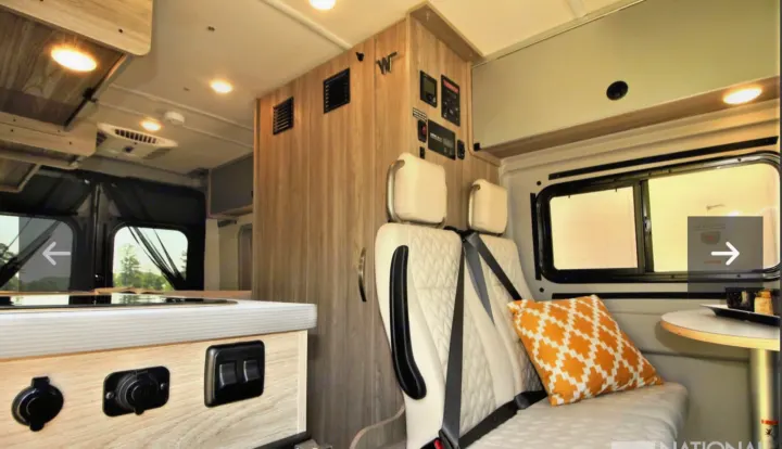 Inside this modern **rv rental**: light wood cabinetry, white seating, compact kitchen, and system controls. Ready for adventure.. Winnebago Solis 2023