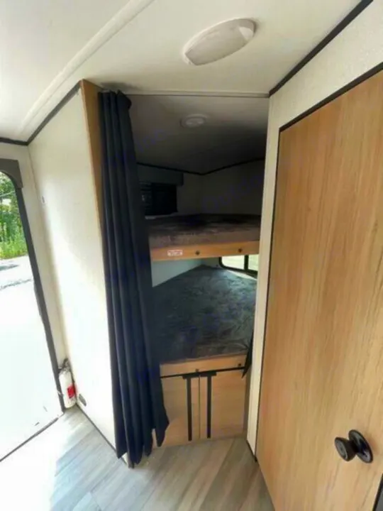 RV rental interior: Bunk beds with privacy curtain, a fire extinguisher near the open doorway, and wood-look flooring.. Cruiser Rv Corp Radiance 2022