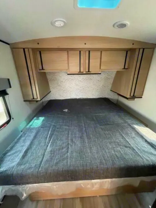 Spacious RV rental bedroom featuring a large bed, overhead cabinets, and bright window for comfortable travel.. Cruiser Rv Corp Radiance 2022