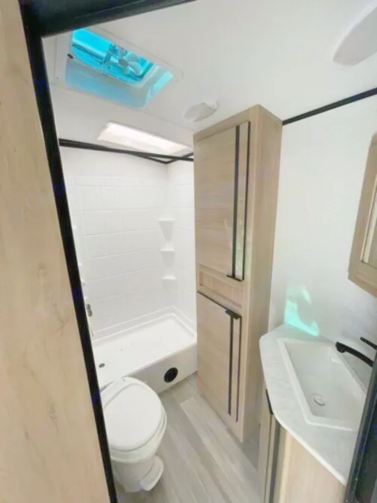 Compact RV rental bathroom showing a white shower, toilet, sink, and wood storage cabinets.. Cruiser Rv Corp Radiance 2022