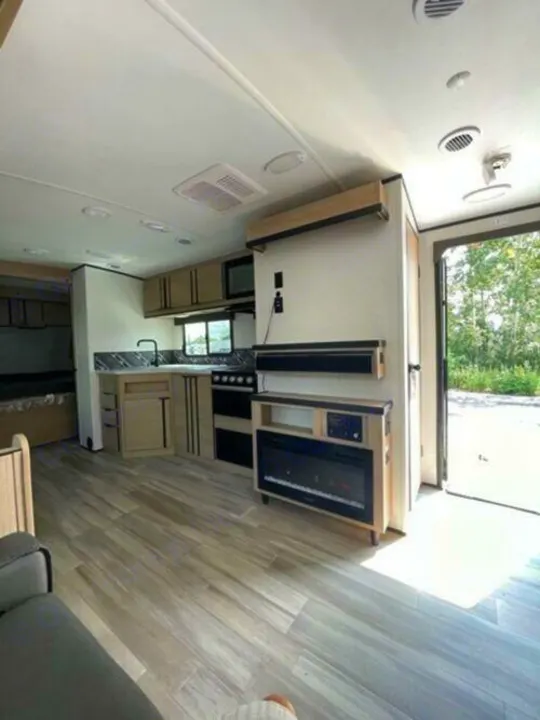 RV rental with a spacious, modern interior. Features include a full kitchen, entertainment center with a fireplace, and light wood flooring.. Cruiser Rv Corp Radiance 2022