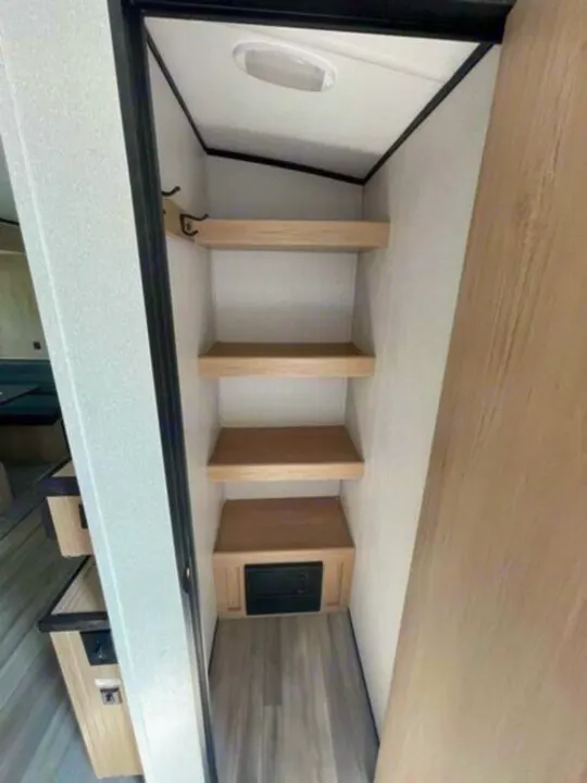 RV rental storage: A compact closet with light wood shelves, wall hooks, and a utility panel at the base. Efficient interior space.. Cruiser Rv Corp Radiance 2022