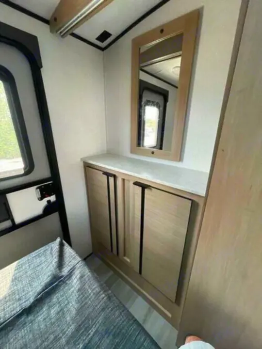 RV rental interior: compact bedroom with window, a bed, and a storage cabinet topped by a mirror.. Cruiser Rv Corp Radiance 2022
