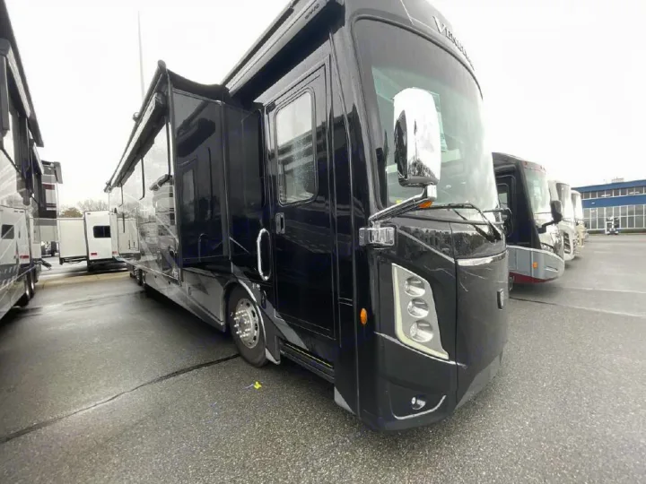 A large, black motorhome with extended slide-outs, parked on a wet lot with other RVs in the background, showcasing luxury RV rental options.. Thor Motor Coach Venetian 2024