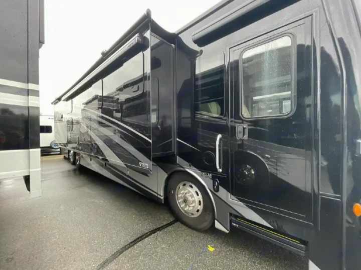 Side view of a luxurious black rv rental motorhome with slide-outs extended, parked on wet pavement.. Thor Motor Coach Venetian 2024