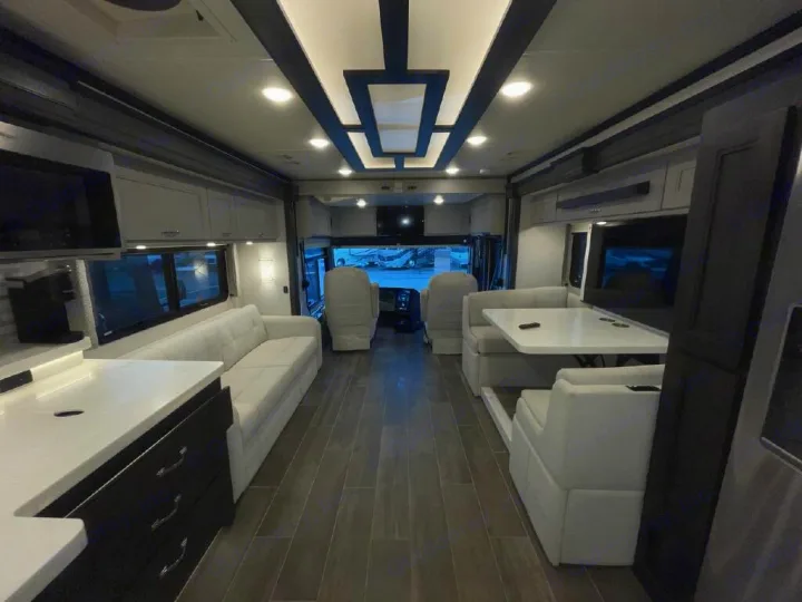 Spacious, modern RV rental interior: bright living area with white seating, dining, kitchen, & driver's cockpit.. Thor Motor Coach Venetian 2024
