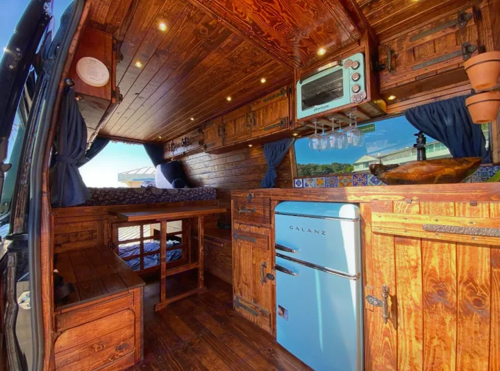Experience a custom RV rental with a rustic wood interior, featuring retro blue kitchen appliances, cozy bed, and detailed craftsmanship.. Mercedes-Benz Sprinter 2016