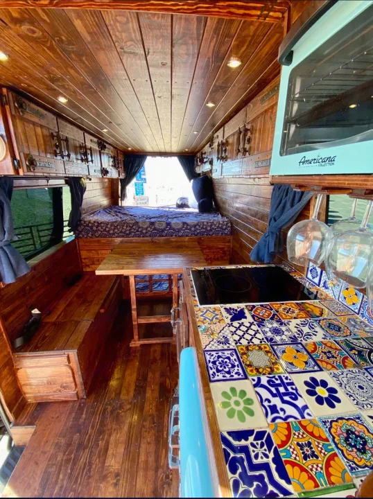 Cozy wood-paneled rv rental: full kitchen with colorful tiles, bed, and dining. Ideal for van life.. Mercedes-Benz Sprinter 2016