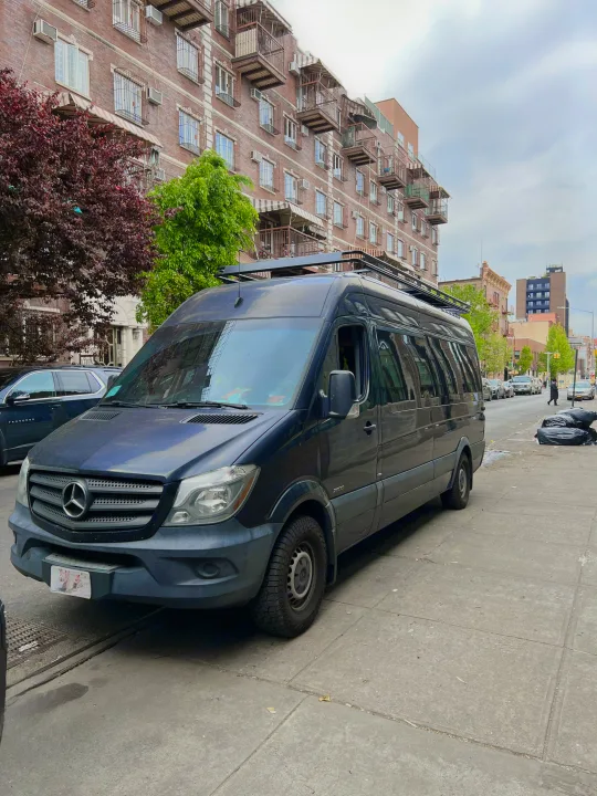 A dark blue Mercedes Sprinter van, ideal for RV rental adventures, parked on a city street with buildings.. Mercedes-Benz Sprinter 2016