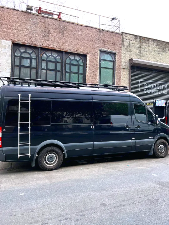 Black Mercedes Sprinter RV rental with roof rack and ladder, parked at Brooklyn Campervans, ready for adventure.. Mercedes-Benz Sprinter 2016