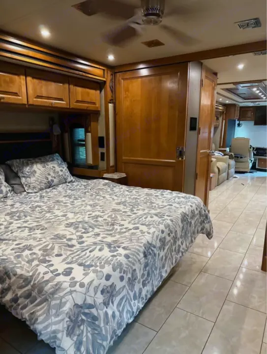 Spacious RV rental interior: bedroom with patterned bedding, wood cabinets, and tile floor extending to living area.. Tiffin Motorhomes Phaeton 2019