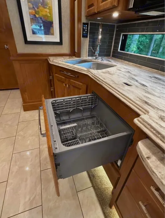 RV rental kitchen: modern counter, double sink, and an open, pull-out drawer dishwasher with visible racks.. Tiffin Motorhomes Phaeton 2019