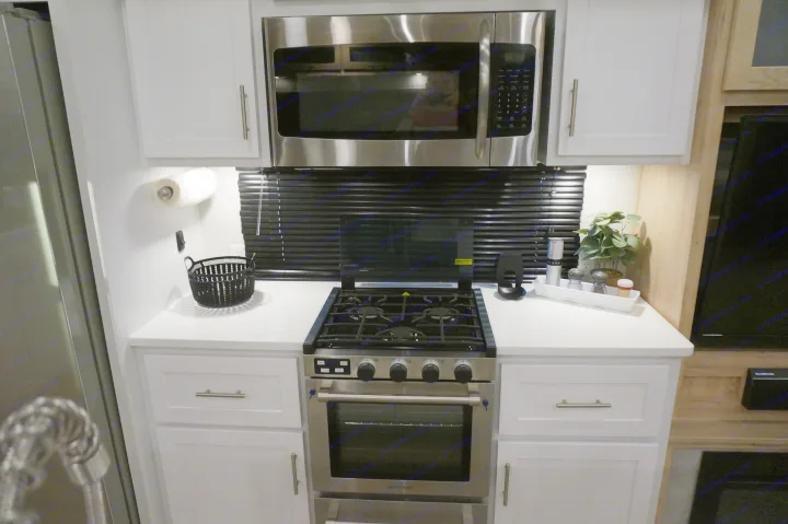 Modern RV rental kitchen featuring stainless steel microwave, gas range, oven, white cabinets & countertops for road trips.. Alliance RV Avenue 2023