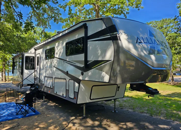 Enjoy an Alliance Avenue fifth wheel rv rental on a sunny day at a campsite, featuring an outdoor mat and chair.. Alliance RV Avenue 2023