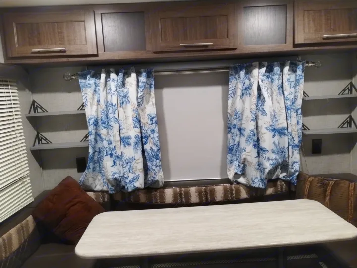 RV rental interior: Wooden cabinets, blue floral curtains, a sturdy table, and comfortable dinette seating.. Crossroads RV Z-1 Lite 2018