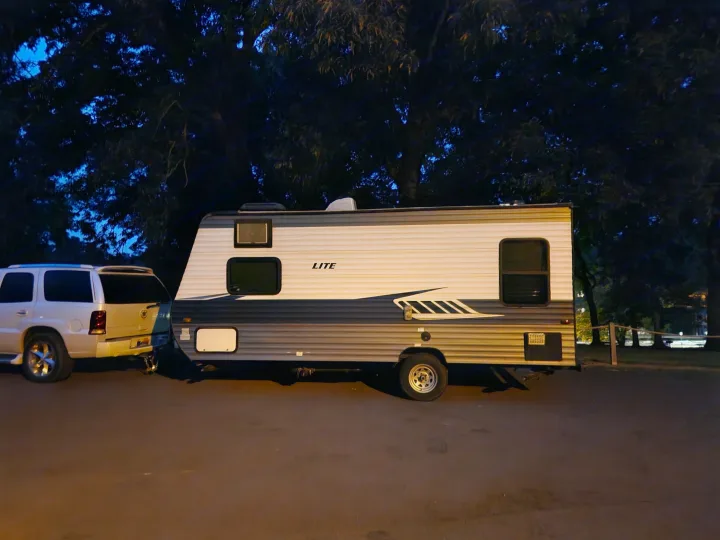 An RV rental hooked to a white SUV, parked at night under dark trees, ready for a leisure travel adventure.. Crossroads RV Z-1 Lite 2018