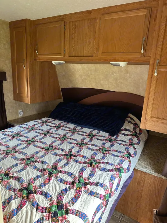 RV rental bedroom with a colorful wedding ring quilt on the bed, flanked by wood overhead cabinets and a built-in headboard.. Jayco Jay Flight 2009