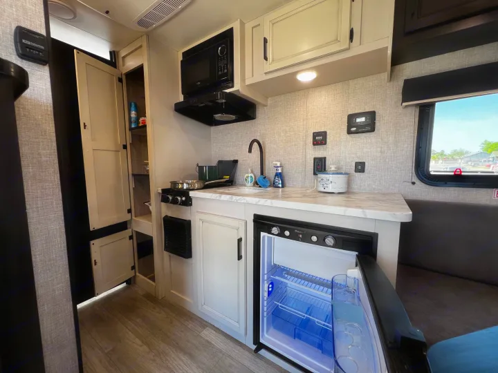 Bright RV rental kitchen with microwave, cooktop, sink, and open fridge showing its blue light, ready for camping.. Jayco Jay Flight SLX Baja Edition 2023