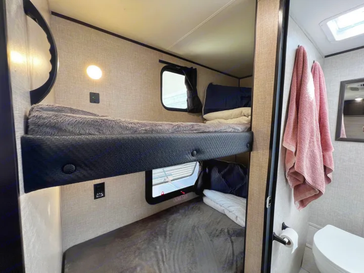 Modern RV rental interior: comfortable bunk beds with personal lighting, USB chargers, and windows, plus a connected bathroom.. Jayco Jay Flight SLX Baja Edition 2023