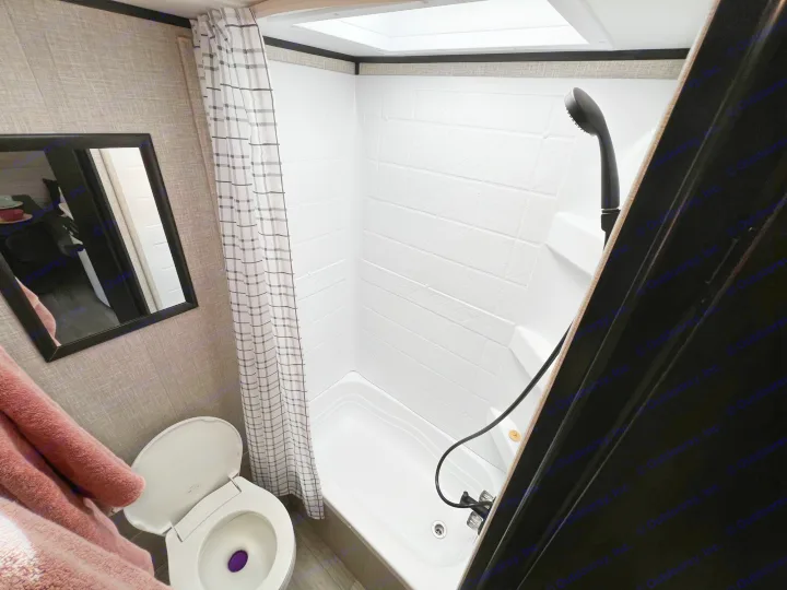 Bright RV rental bathroom with a clean shower/tub, toilet, plaid curtain, and skylight. Mirror and pink towel visible.. Jayco Jay Flight SLX Baja Edition 2023