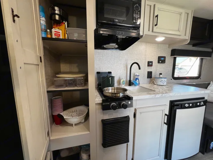 Compact RV rental kitchen with stove, sink, microwave, fridge, and open pantry. Perfect for travel adventures.. Jayco Jay Flight SLX Baja Edition 2023