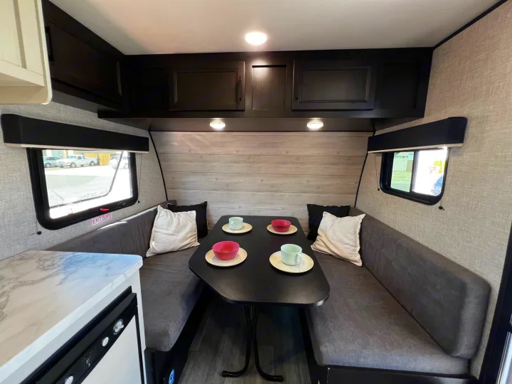 Step inside this modern RV rental showcasing a compact dinette with table, benches, and overhead cabinets, plus a small kitchen.. Jayco Jay Flight SLX Baja Edition 2023