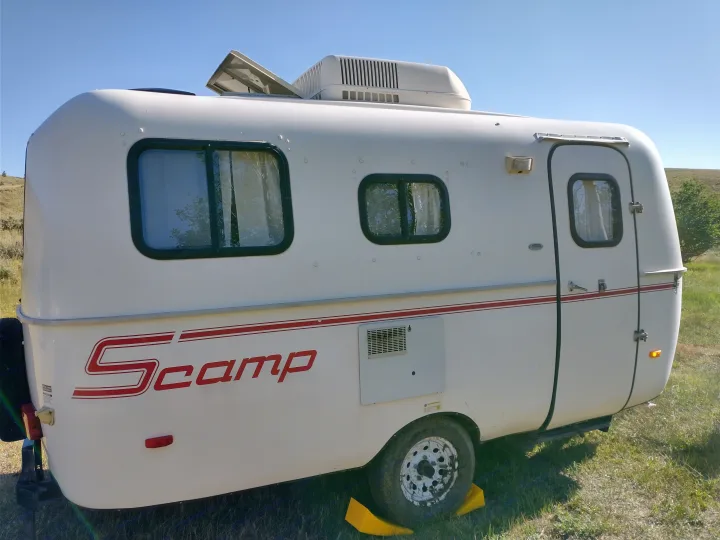 White Scamp travel trailer RV rental, parked on grass. Side view highlights windows, door, and roof AC unit.. Scamp Scamp Trailer 2011
