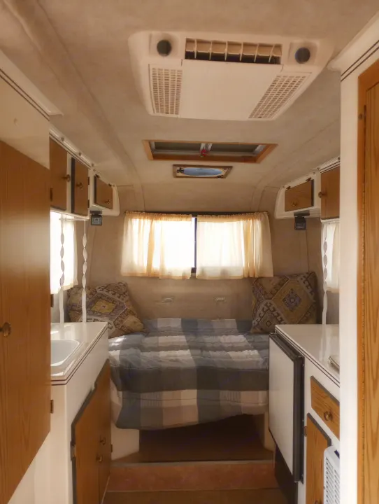 Interior view of a clean RV rental, featuring a bed, small kitchen, overhead cabinets, and air conditioning.. Scamp Scamp Trailer 2011