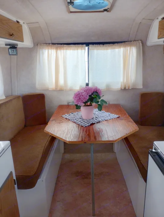 Inside a charming RV rental, featuring a dinette with a pink flower pot, cozy benches, and sunlit windows.. Scamp Scamp Trailer 2011