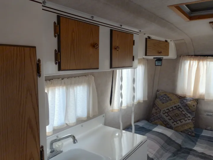 Inside a cozy RV rental: compact kitchen with sink, wooden cabinets, and a comfortable sleeping area. Ideal for road trips.. Scamp Scamp Trailer 2011