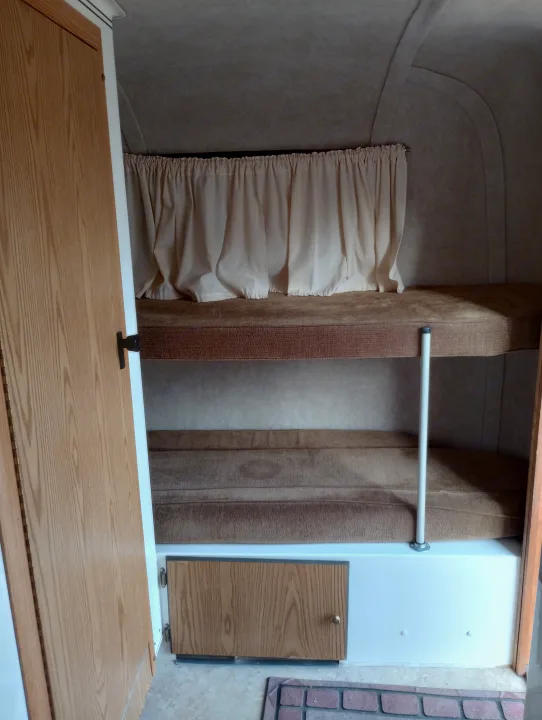 Cozy RV rental bunk beds with privacy curtain, wood door, and cabinet, ideal for travel.. Scamp Scamp Trailer 2011