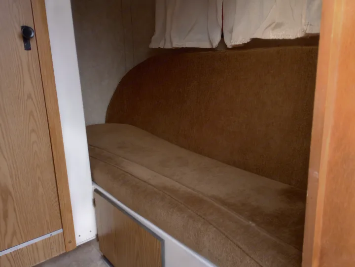 Cozy brown bench seating and sleeping area inside an RV rental, with cabinets below and privacy curtains above. Wood accents on left.. Scamp Scamp Trailer 2011