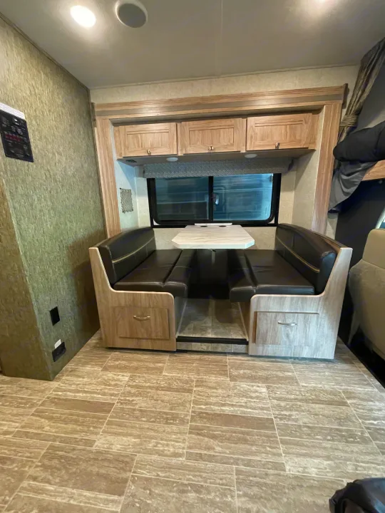 RV rental interior featuring a cozy dinette with black benches, a white table, and overhead cabinets for storage.. Forest River Sunseeker 2018