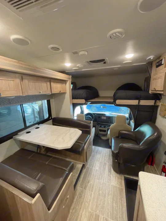 This RV rental interior features a brown dinette, light wood cabinets, overhead sleeping bunk, and driver's cockpit.. Forest River Sunseeker 2018