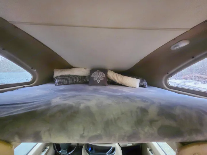 Inside an RV rental: cozy cab-over sleeping bunk with a plush grey bed and decorative pillows. View from above the driver's seat.. Thor 2012 Thor 19G 2012