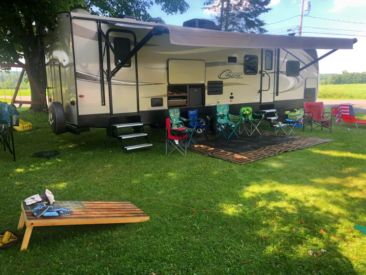 Spacious Cougar RV rental with extended awning, outdoor kitchen, camping chairs, and cornhole setup on a sunny lawn.. Keystone RV Cougar X-Lite 2018