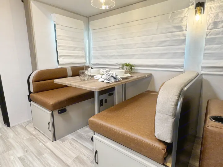 Spacious RV rental dinette with cozy brown seating, a wood-grain table set with dishes, and light-filtering window blinds.. Forest River Vibe 34BH 2024