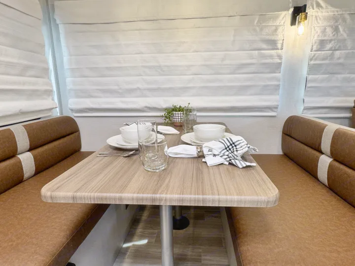 An RV rental's cozy dinette, featuring a wooden table, brown benches, and full place settings for meals.. Forest River Vibe 34BH 2024