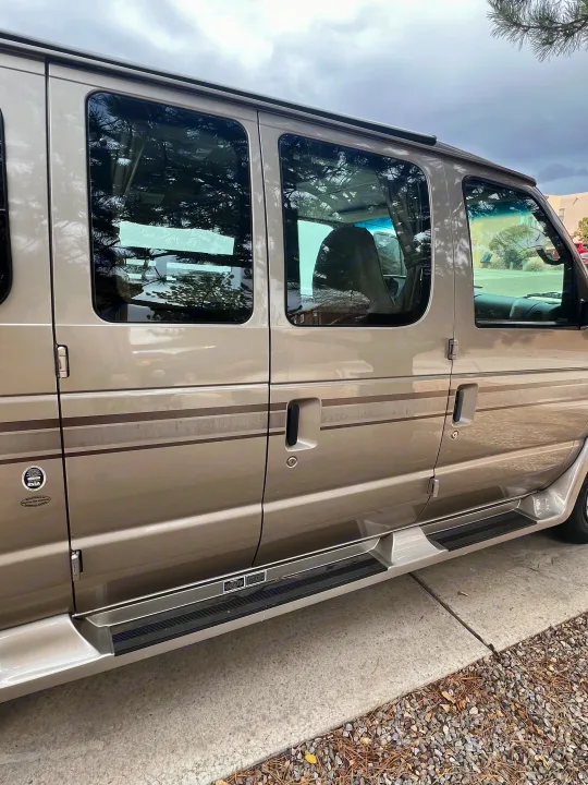Side view of a beige RV rental van, showing its windows, passenger doors, and running boards. Ideal for road trips.. Ford Pleasure Way Xl Rd Widebody 2002