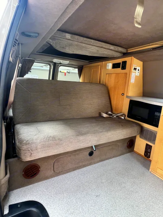 Interior of a practical rv rental with a large bench seat, overhead bunk, and built-in kitchenette including a microwave.. Ford Pleasure Way Xl Rd Widebody 2002