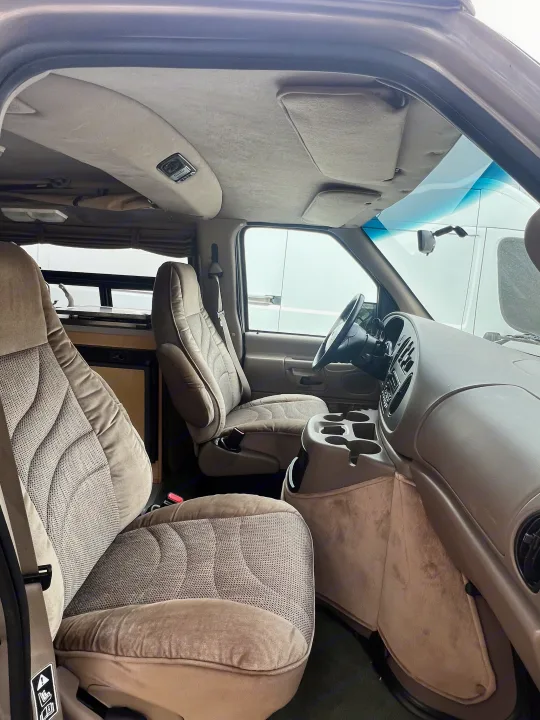 Detailed RV rental interior: beige seats, dashboard, and a view into the rear camper area with a sink.. Ford Pleasure Way Xl Rd Widebody 2002