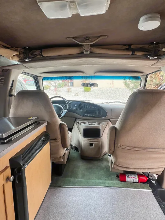 Inside this rv rental, view forward: tan interior, driver & passenger seats, dashboard, and a compact kitchen setup on left.. Ford Pleasure Way Xl Rd Widebody 2002