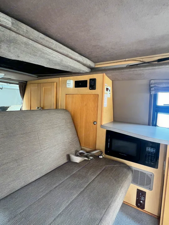 RV rental: Pop-up camper interior with bench seat, microwave, and wood storage. Functional living space.. Ford Pleasure Way Xl Rd Widebody 2002