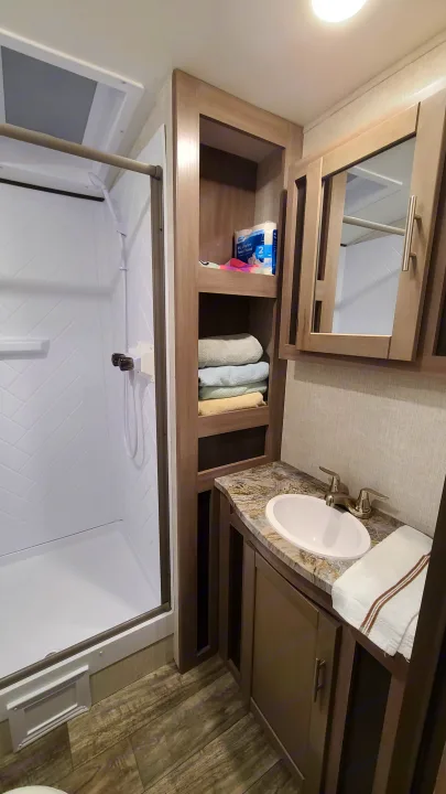 This RV rental bathroom features a compact shower, vanity with sink, mirror, and shelves with towels & RV toilet paper.. Crossroads RV Sunset Trail Super Lite 2022