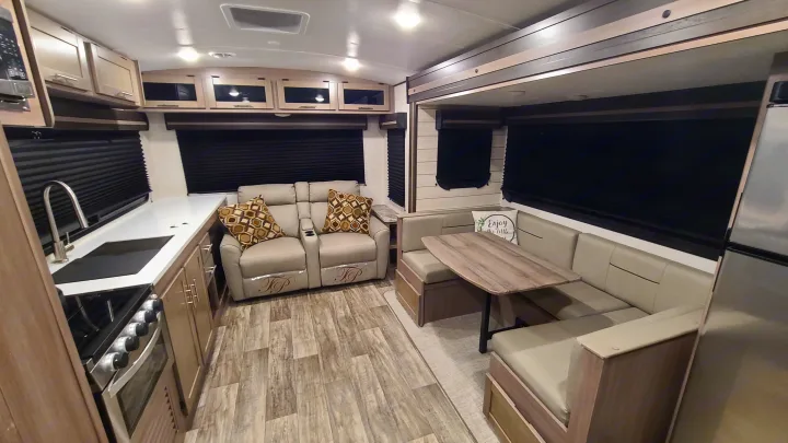 Spacious RV rental interior: modern kitchen with stove, twin recliners, and a U-shaped dinette.. Crossroads RV Sunset Trail Super Lite 2022