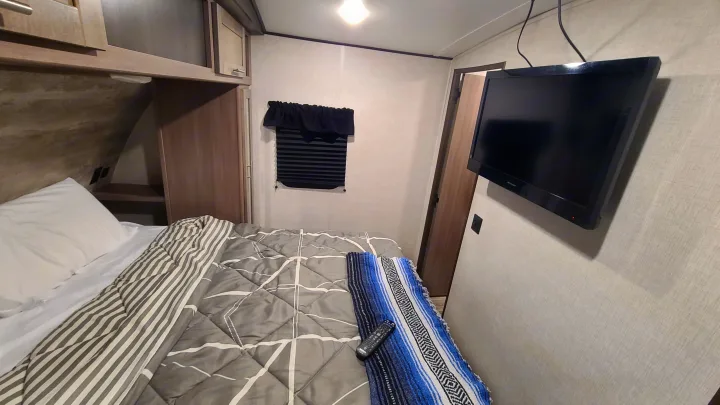 Cozy RV rental bedroom showing a bed with patterned bedding, wall-mounted TV, and window. Ideal for travel.. Crossroads RV Sunset Trail Super Lite 2022